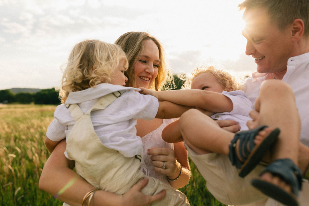 Mother laughing with two children in field during family photoshoot sunset light