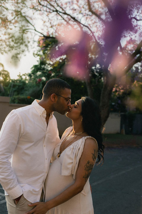Expectant mother standing under purple jacaranda trees during outdoor maternity photoshoot Pretori